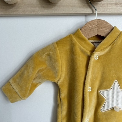 Macacão de bebé amarelo com estrela branca pendurado num cabide de madeira