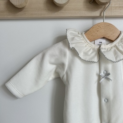 Macacão bebé branco com gola folho e botões pendurado em cabide de madeira