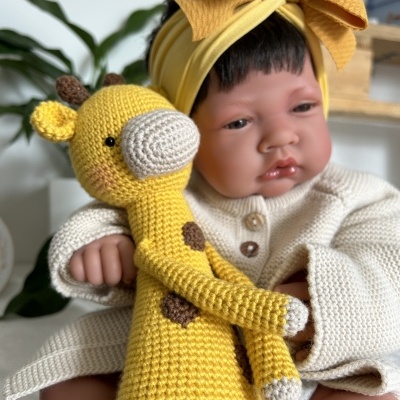 Boneca bebé com roupinha creme e touca amarela segurando giraffa de croché