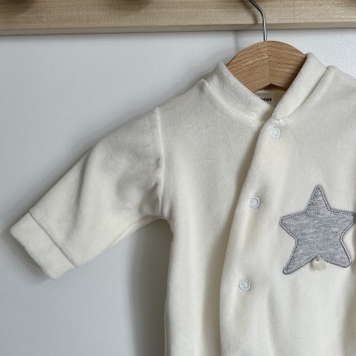 Roupa de bebé branca com estrela cinzenta pendurada em cabide de madeira