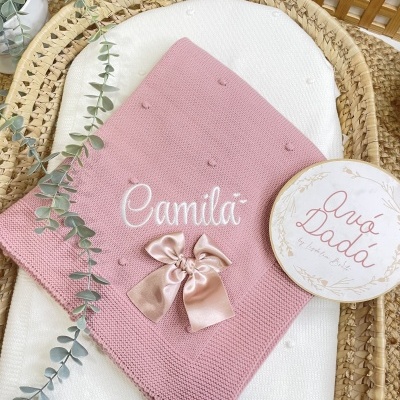 Cobertor bebé cor-de-rosa em malha com laço e bordado em suporte de vime com planta e cartão.