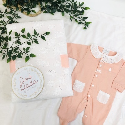 Macacão de bebé cor-de-rosa com detalhes brancos e manta branca com planta verde e etiqueta redonda