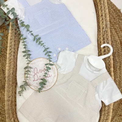 Dois macacões de bebé às riscas azul e bege com t-shirts brancas, expostos num berço de rattan com ramo verde e placa Avó Dada.