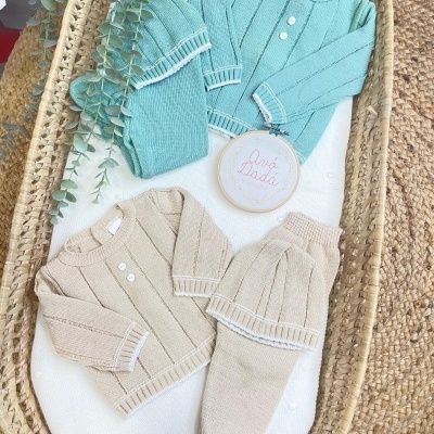 Conjuntos de roupa de bebé em malha azul e bege com detalhes brancos em cesta de verga