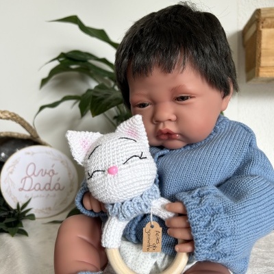 Boneco bebé com camisola azul segurando brinquedo de madeira com gato de croché