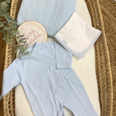 Conjunto de bebé azul claro com babygrow, manta e fralda numa cesta de vime