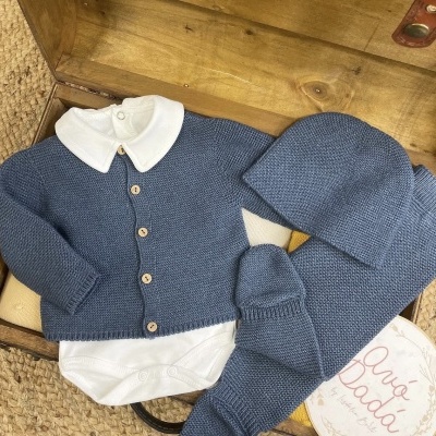 Conjunto de roupa de bebé azul com body branco e acessórios sobre mala de madeira