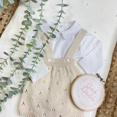 Roupa de bebé branca e bege com planta verde e bastidor bordado