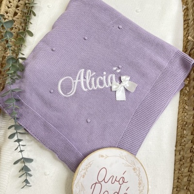 Manta de bebé lilás bordada com o nome Alicia e cesto com placa Avó Dadá