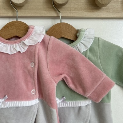 Dois macacões infantis em veludo rosa e verde com gola branca na parede