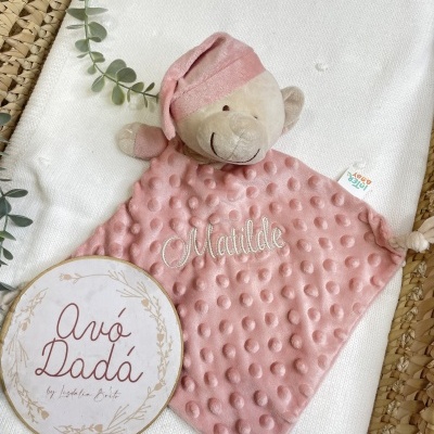 Manta rosa com ursinho de peluche e bordado Matilde, quadro decorativo com texto Avó Dadá, sobre fundo branco e cesta de palha.