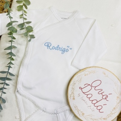 Body de bebé branco com bordado azul Rodrigo e plantas verdes ao lado