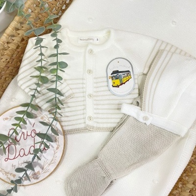 Conjunto de roupa de bebé branca e bege com etiqueta baby maiors num cesto de palha com planta artificial