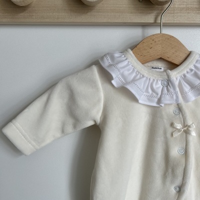macacão de bebé creme com gola branca e botões azuis pendurado em cabide de madeira