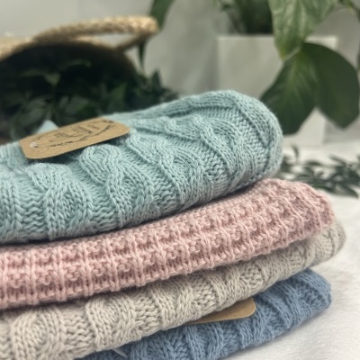 Conjunto de quatro peças de malha colorida dobradas com padrão trançado e ponto de malha, plantas ao fundo