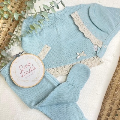 Conjunto azul de bebé com rendas bege e laço, gorro, camisola e calças.