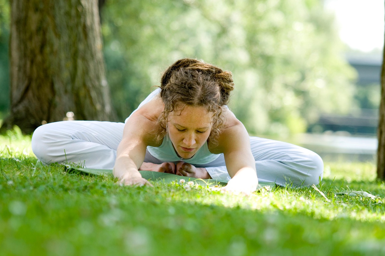 Mulher a fazer yoga ao ar livre, vestindo roupa branca, num ambiente natural com relva e árvores