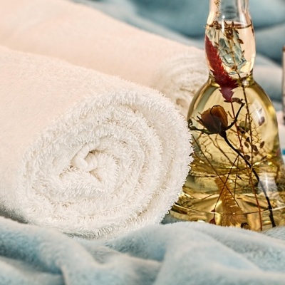 Toalha branca enrolada, frasco de óleo aromático com flores, frascos de aromaterapia em tecido azul