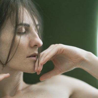 Mulher com olhos fechados e mãos no rosto com fundo verde.