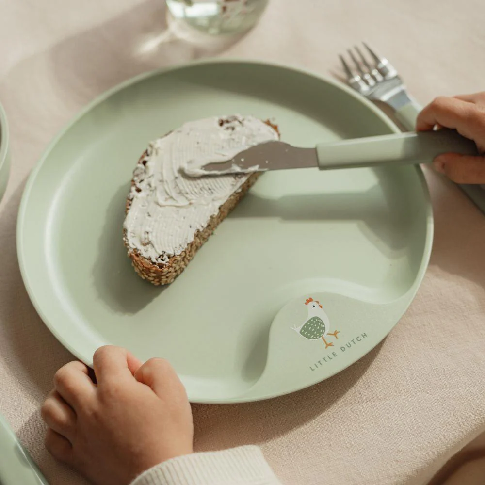 Prato verde claro com divisão e desenho de galinha, pão com creme num ambiente de mesa
