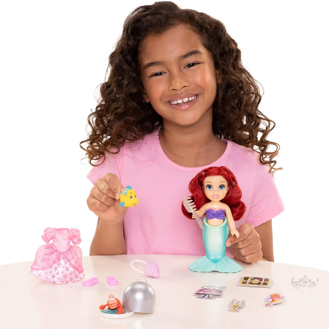 Menina com boneca sereia e acessórios de brincadeira numa mesa branca