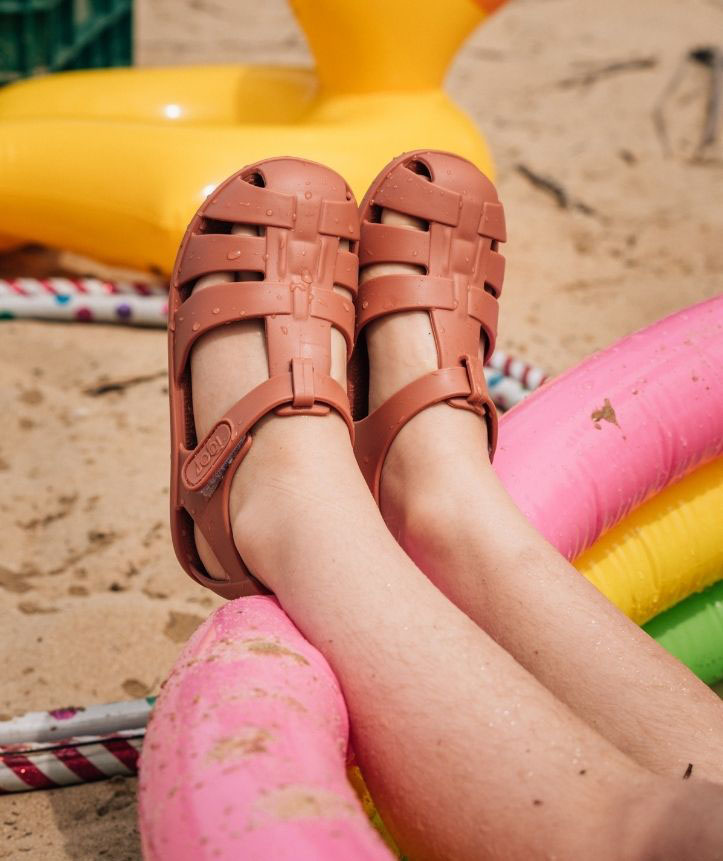 Calçado infantil tipo sandália cor de salmão num ambiente de praia