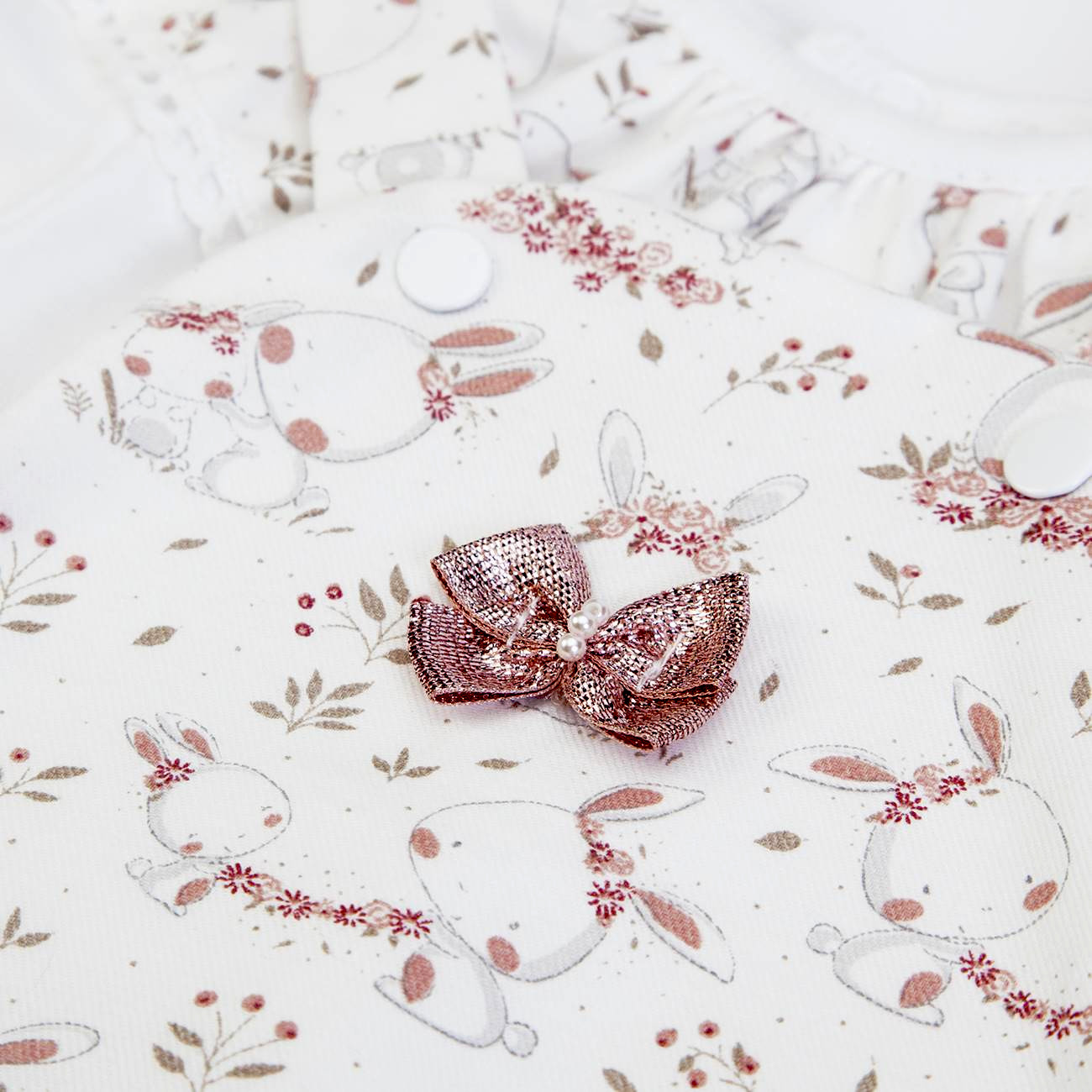 Peça de roupa de bebé branca com estampa de coelhos e flores, com laço rosa brilhante