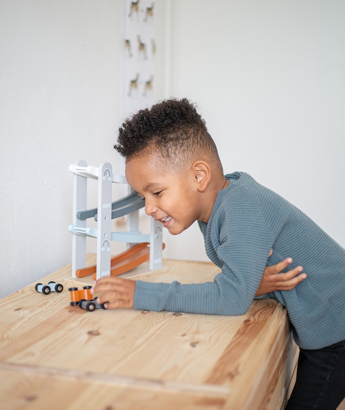 Criança a brincar com carrinhos num cenário de pista de carros de madeira