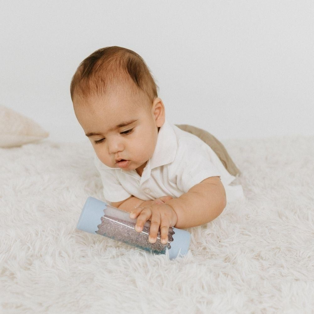 Bebé vestido de branco segurando brinquedo azul num tapete branco