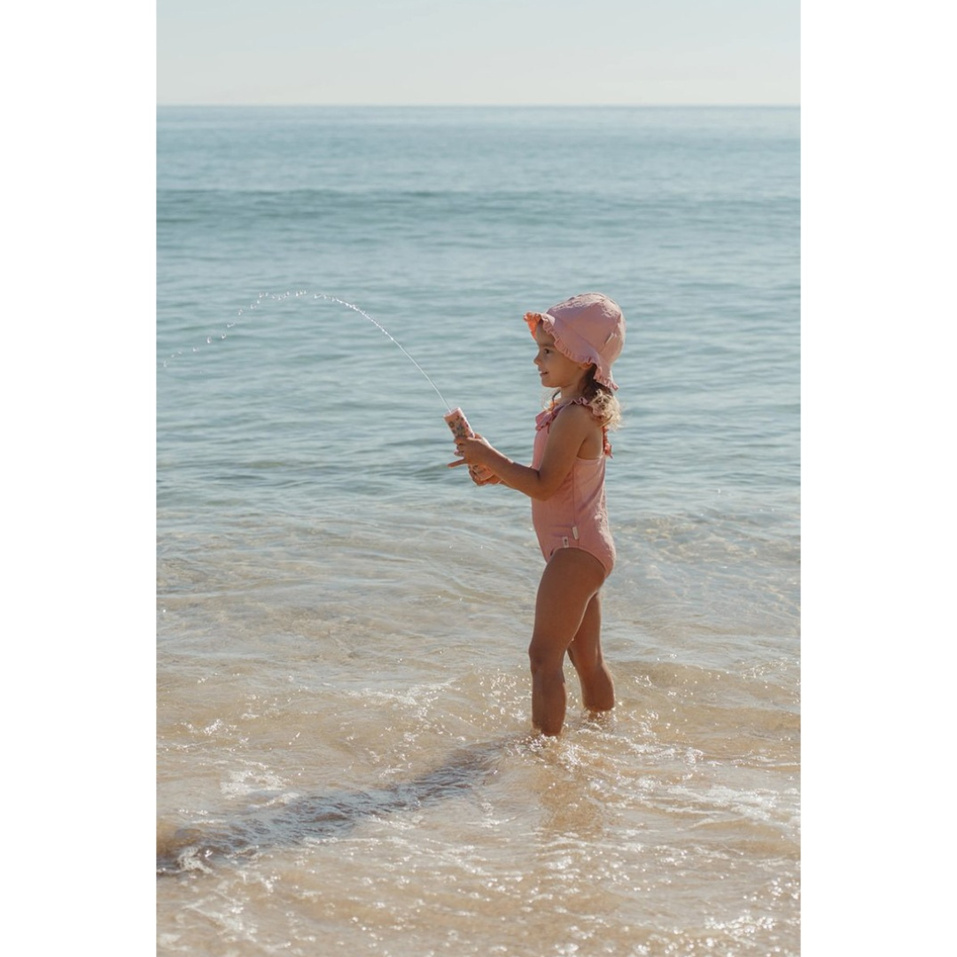 Criança a brincar na praia com fato de banho e chapéu rosa
