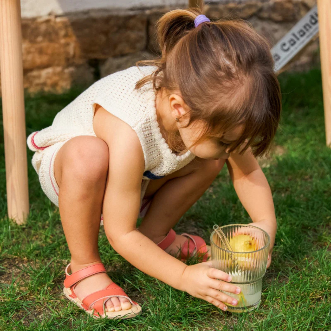 Criança agachada na relva segurando um copo de vidro com fatias de fruta