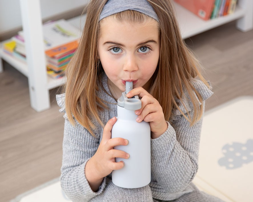 Garota jovem a beber de uma garrafa de água branca com tampa cinzenta e canudo integrado