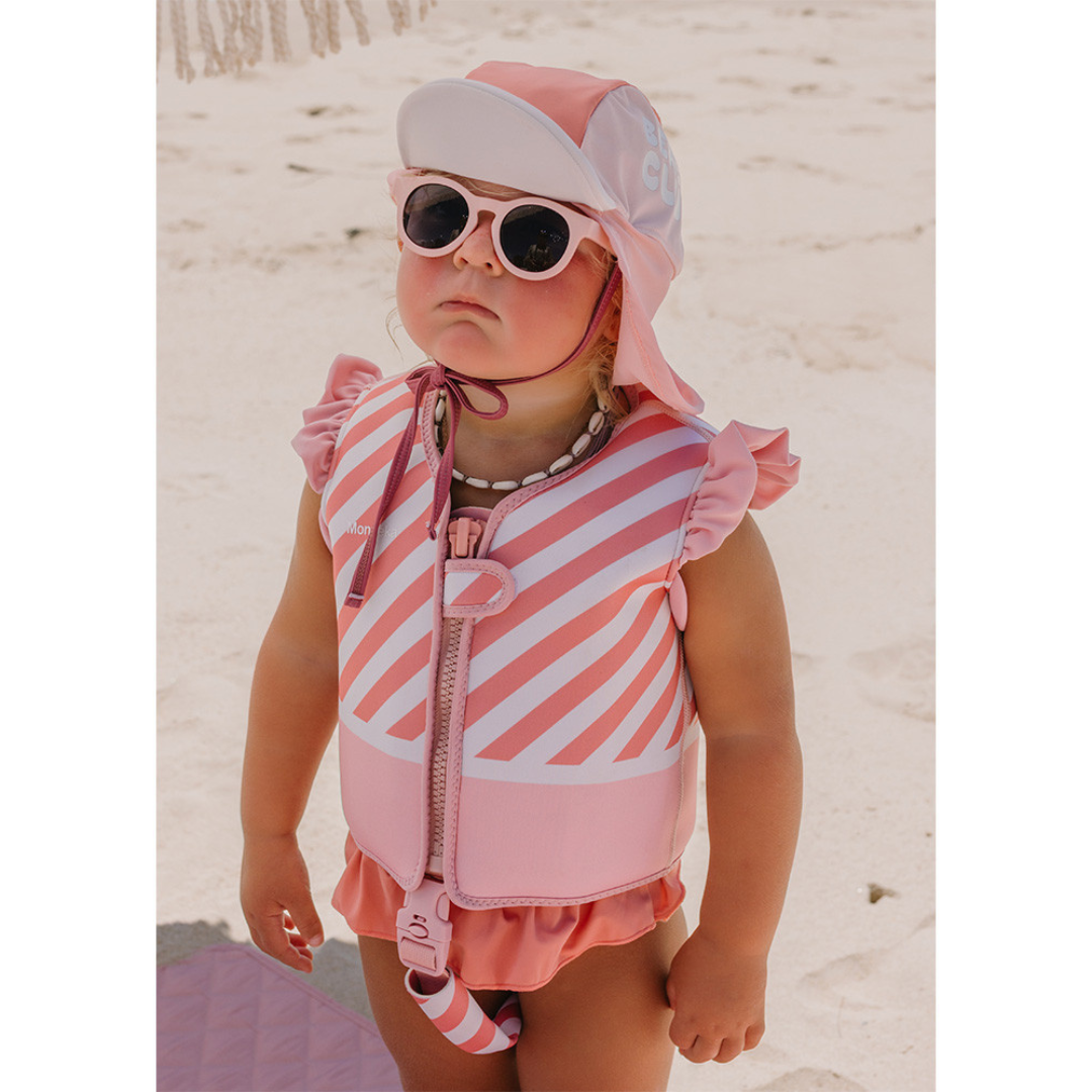 Criança na praia com colete salva-vidas rosa e óculos de sol