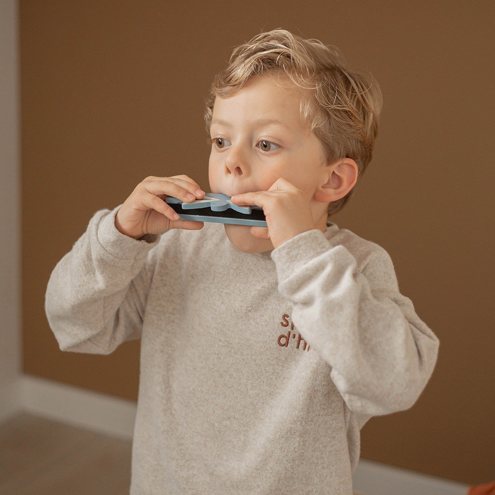 Criança a tocar instrumento musical azul escuro num quarto com parede castanha
