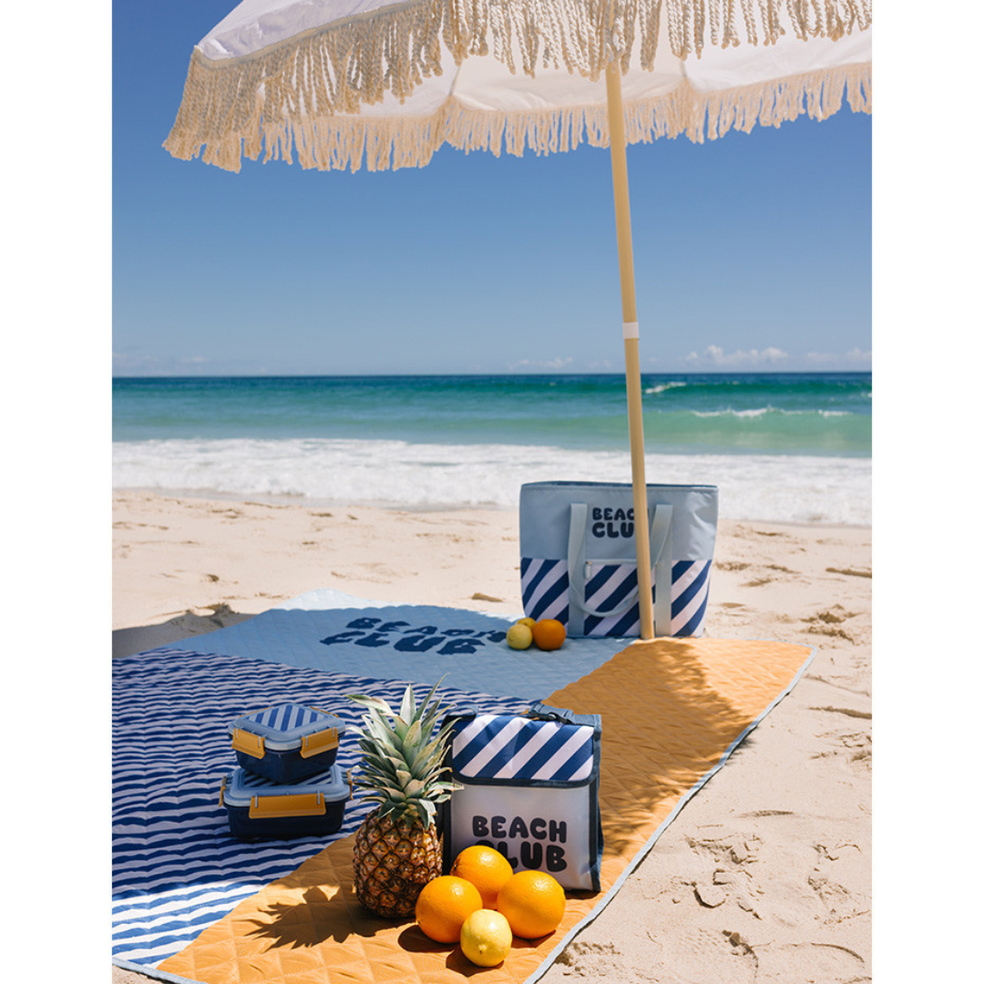 Conjunto de acessórios de praia azul, branco e amarelo com texto BEACH CLUB na areia da praia
