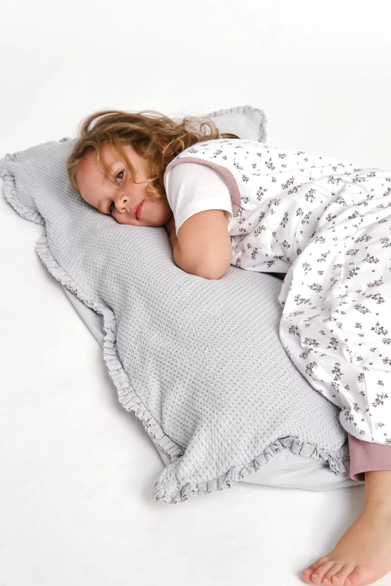 Criança deitada numa almofada cinza com textura de malha e roupa de dormir floral
