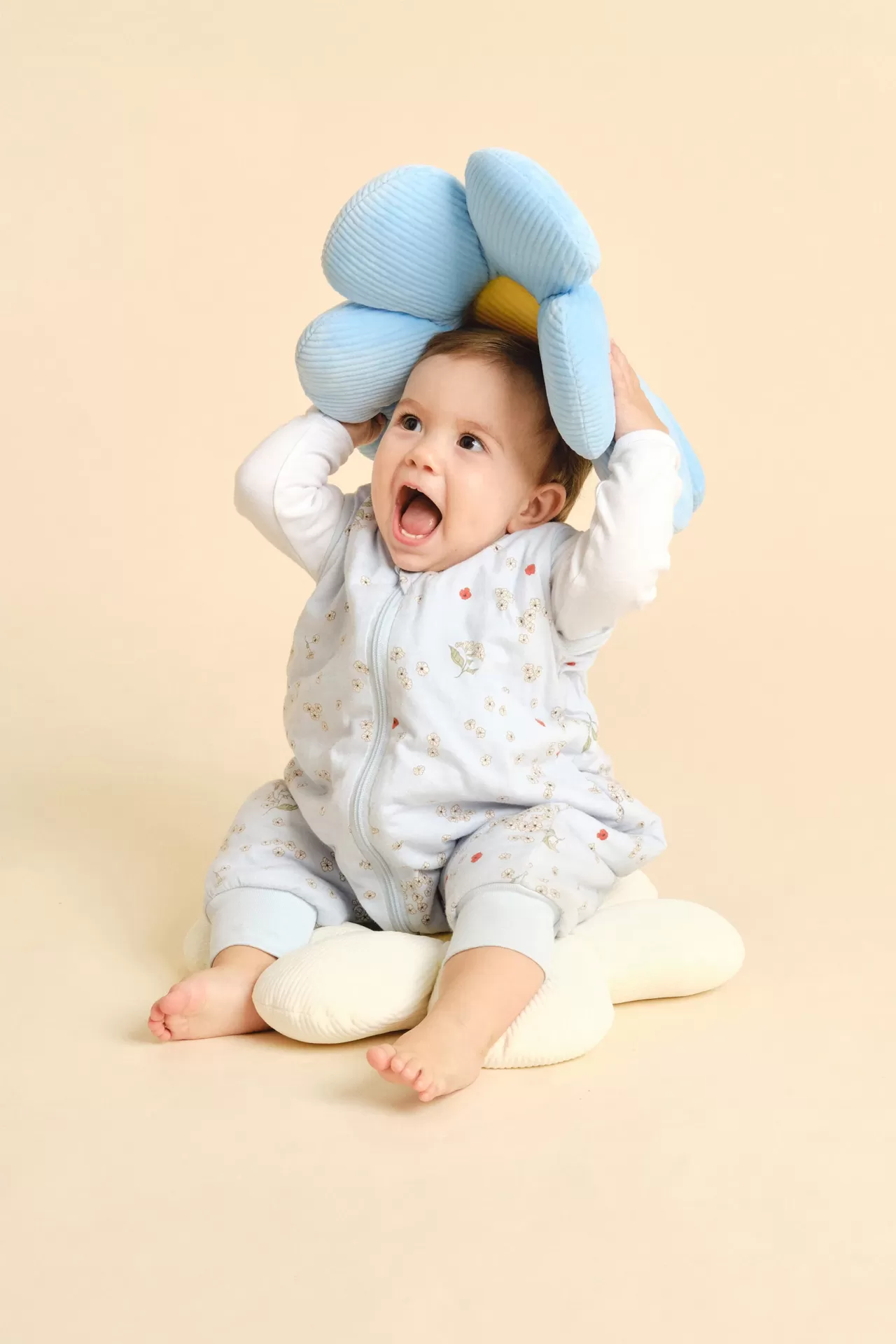 Bebé com roupão azul claro floral sentado sobre almofada em forma de flor