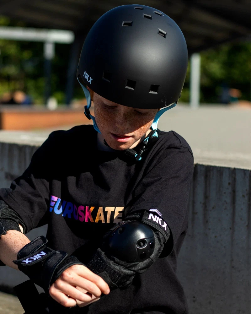 Criança com equipamentos de proteção para skate e roupa preta com texto colorido