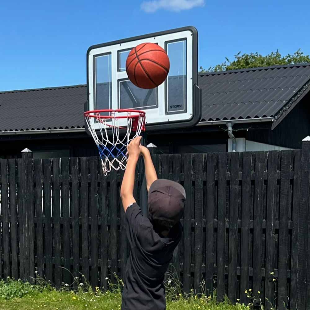 Cesto de basquetebol com aro vermelho e bola a entrar no cesto numa área exterior