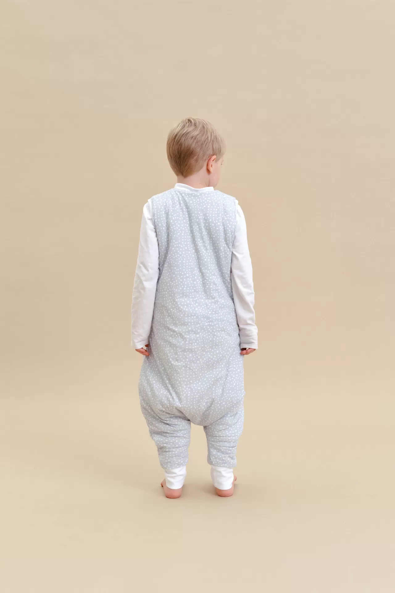 Criança com babygrow cinzento claro com pontos brancos visto de costas