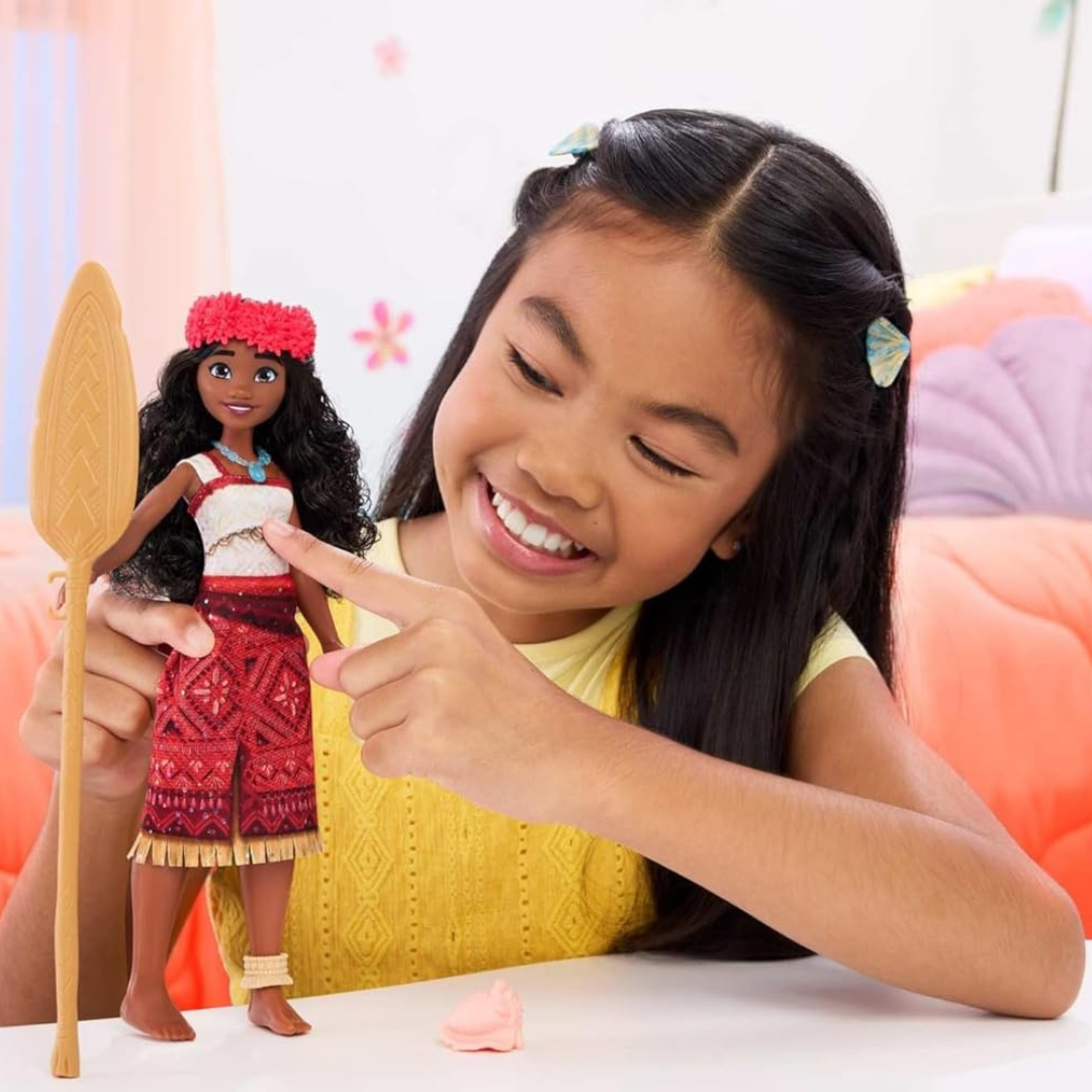 Menina a brincar com boneca vestida com roupa tradicional vermelha e branca, segurando uma pagaia.