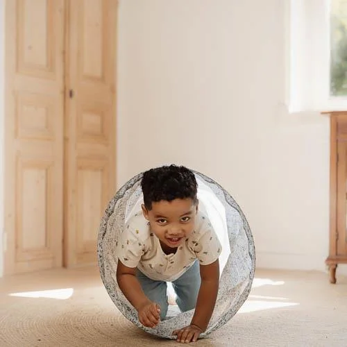 Criança a brincar num túnel de tecido branco com padrão cinza em sala clara