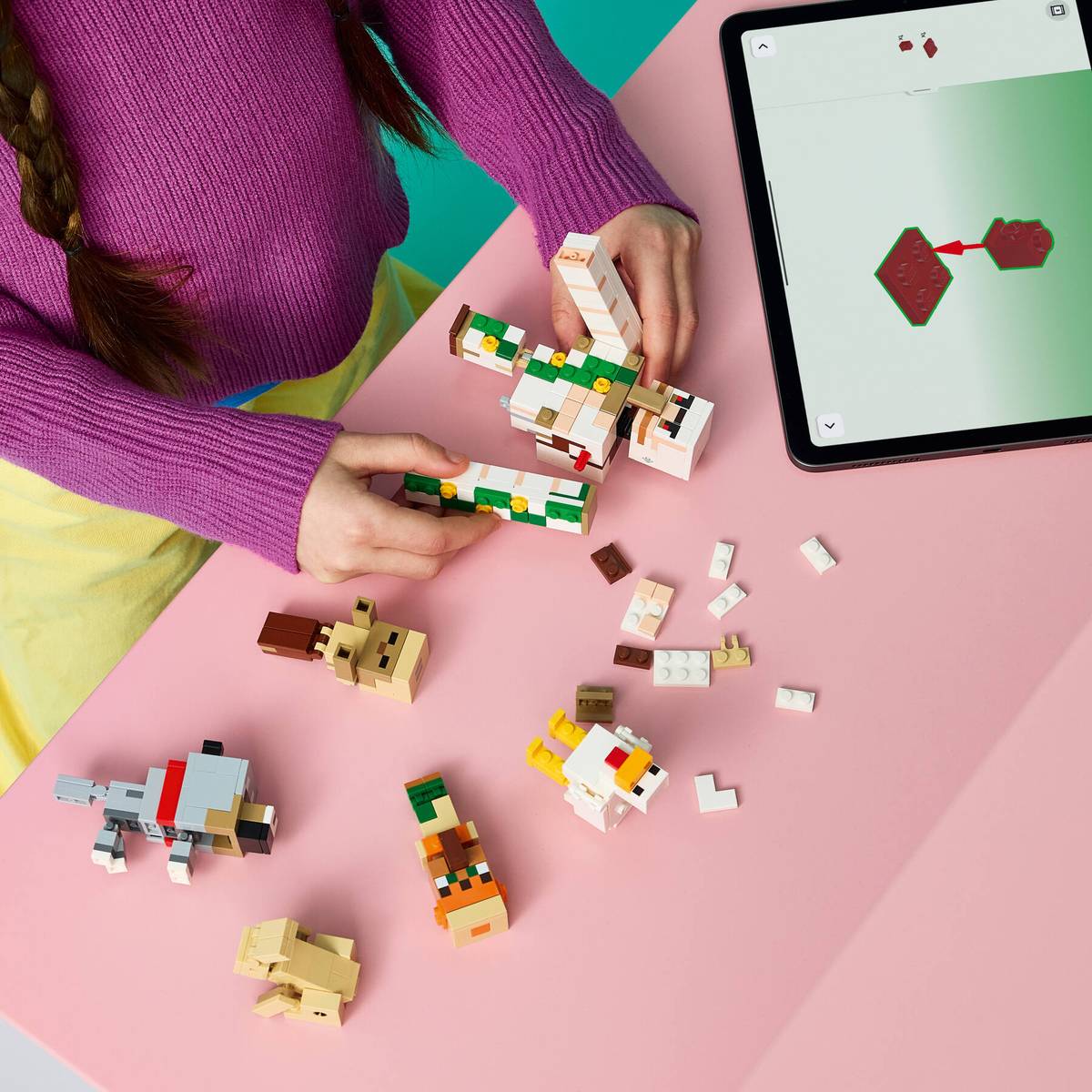Figuras de blocos de construção de animais sobre mesa cor-de-rosa com criança a montar e tablet com instruções