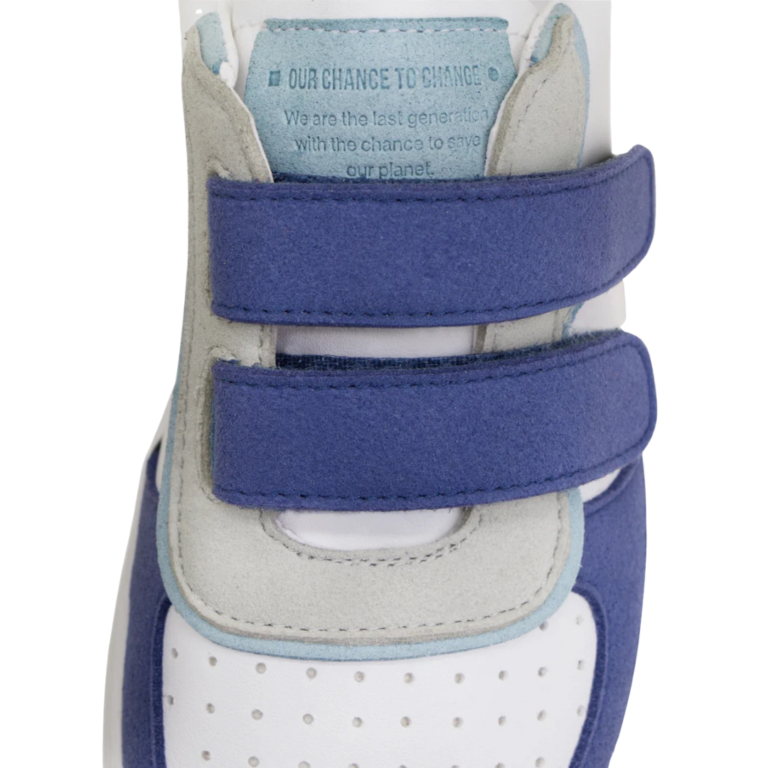 Ténis branco com detalhes azuis e cinza e fecho de velcro com texto na língua.