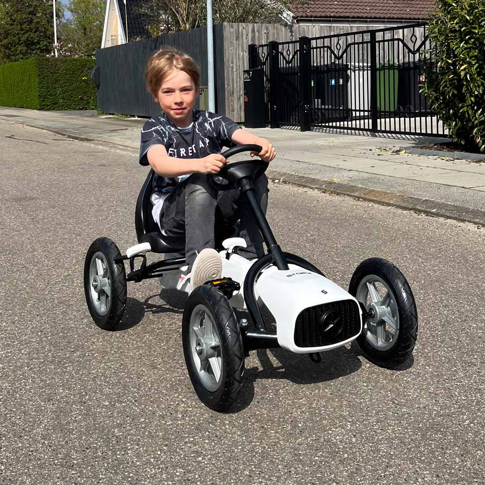 Criança num carrinho de pedal branco e preto numa rua residencial.