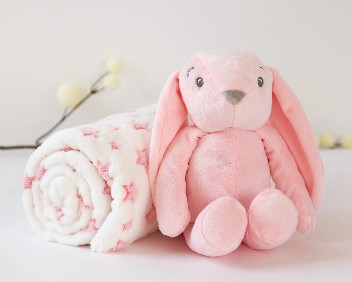 Pelúcia de coelho cor-de-rosa ao lado de manta branca com estrelas cor-de-rosa