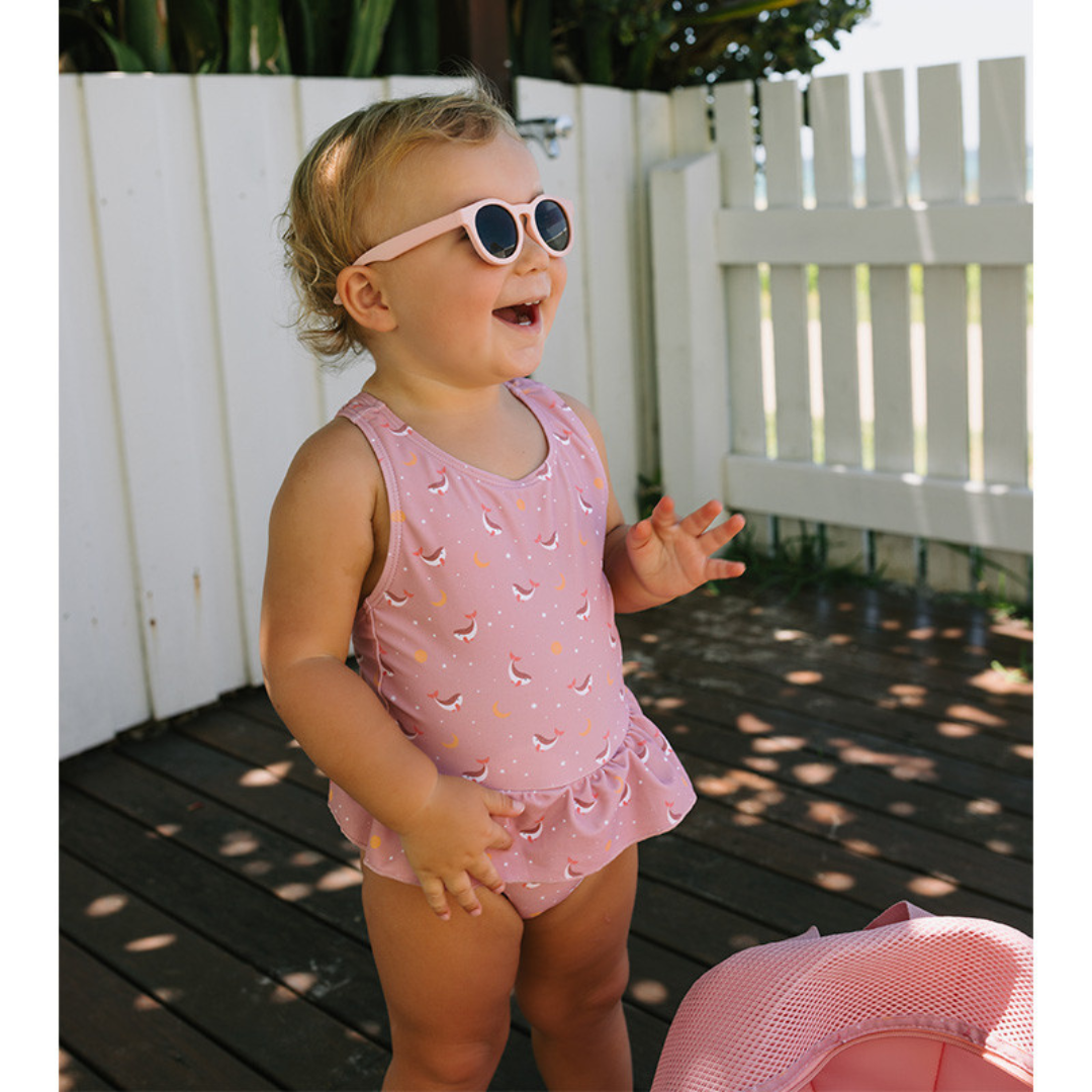 Bébé com fato de banho rosa e óculos de sol