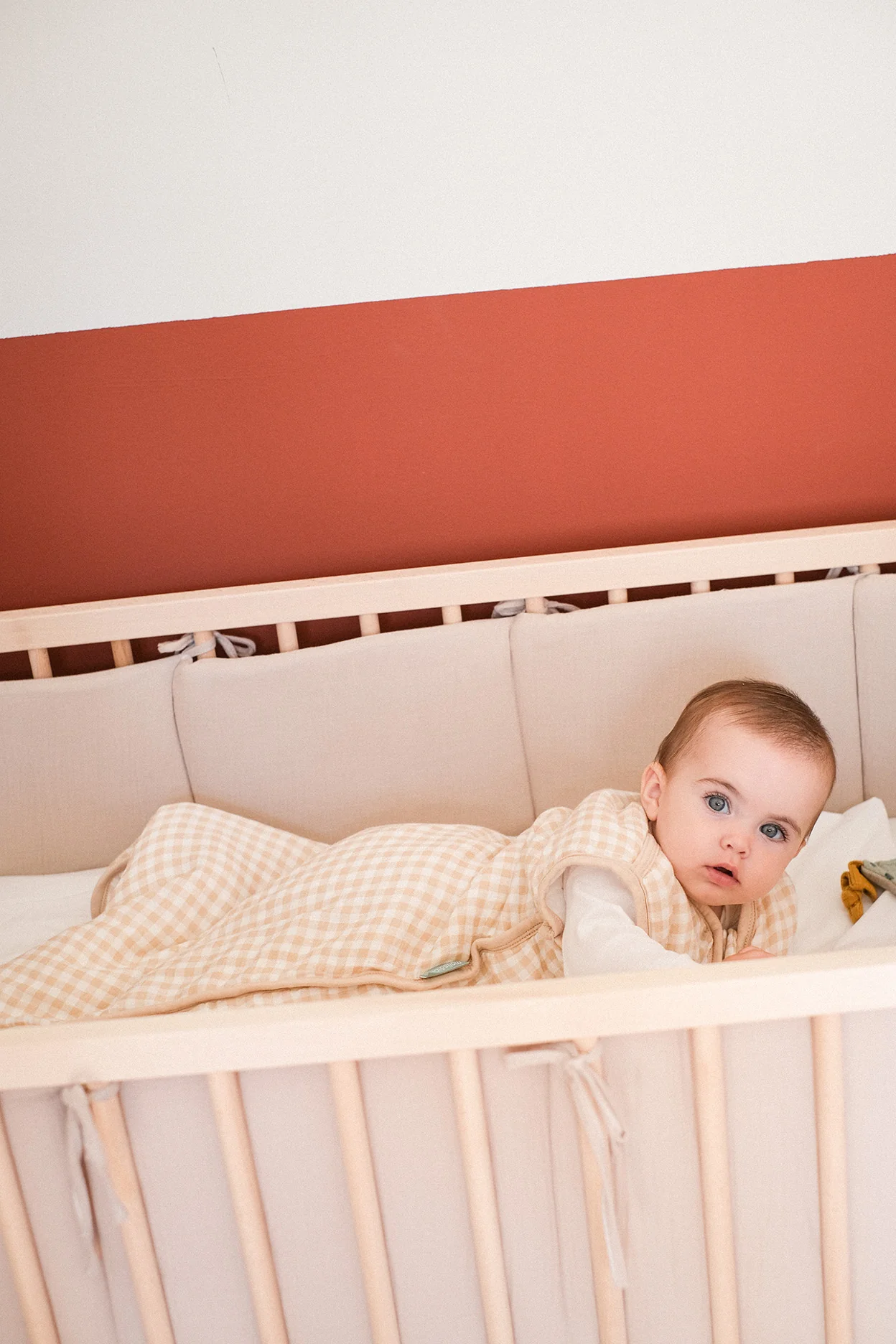 Bebé deitado num berço com saco de dormir xadrez bege e branco