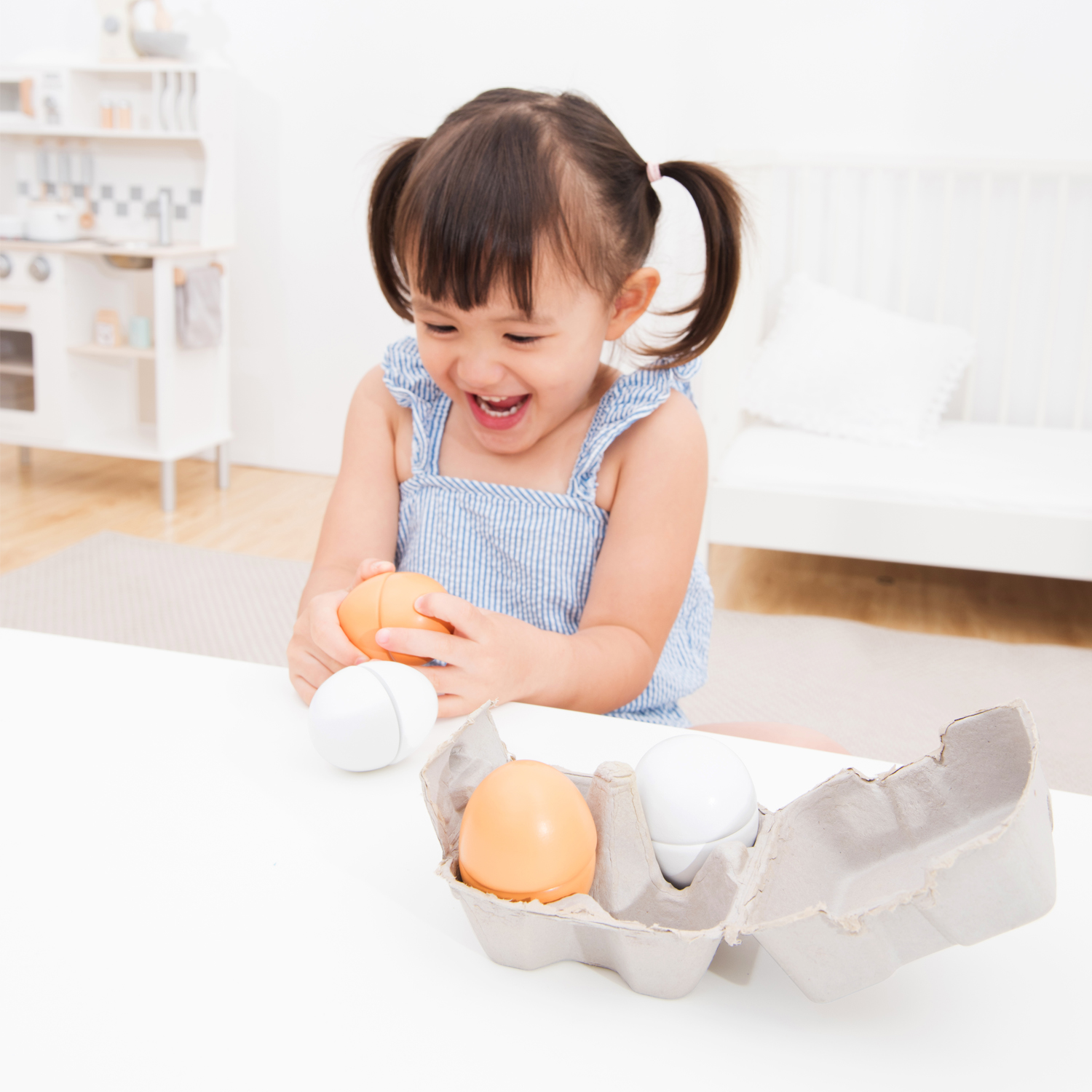 Menina a brincar com ovos de plástico coloridos numa caixa cinzenta sobre mesa branca