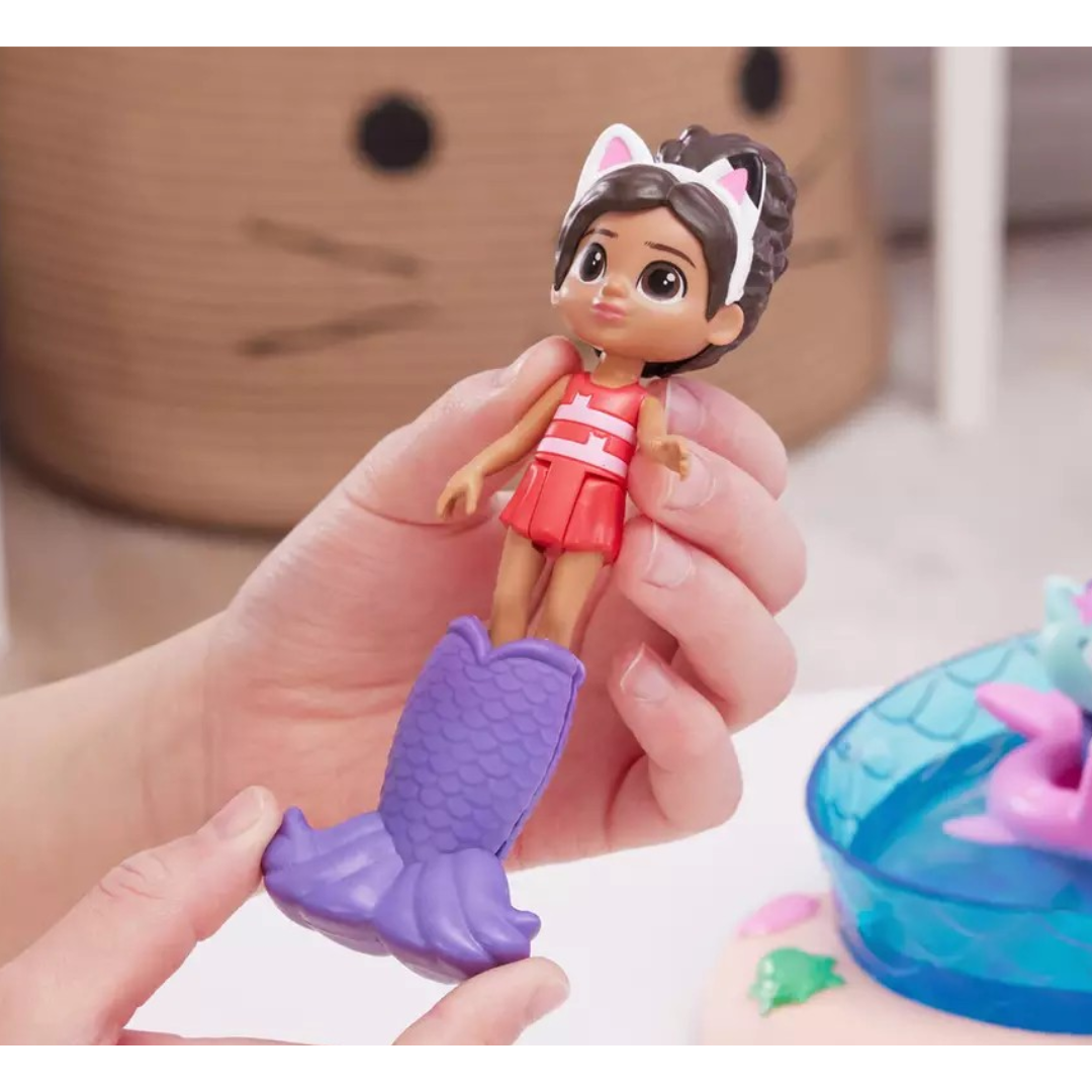 Boneca pequena com cauda de sereia roxa e roupa vermelha, segurada por mãos infantis